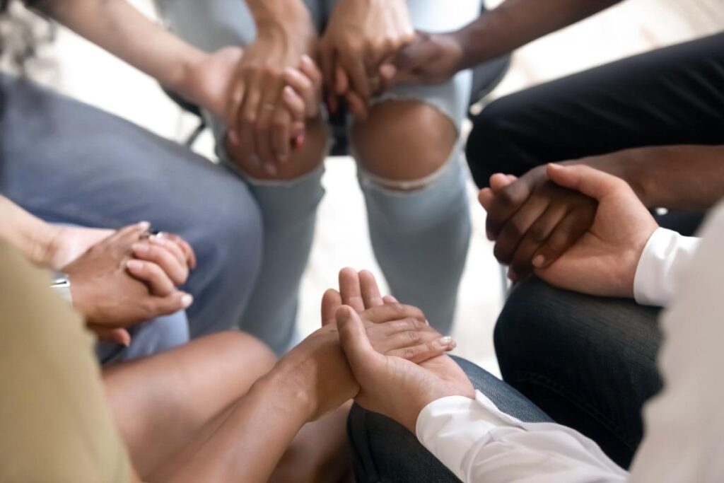 A group of people hold hands and discuss mental health