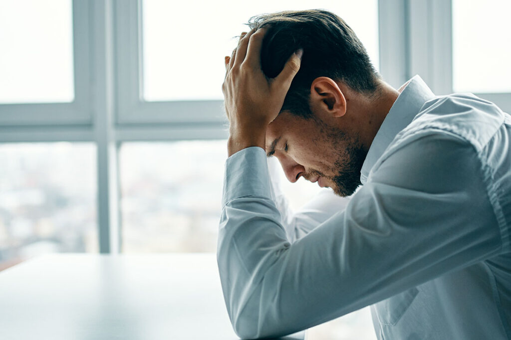 Man with head in hands considering the signs of alcoholism